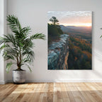 Lone hiker standing on a rocky cliff edge overlooking a forested valley at sunset with golden skies.